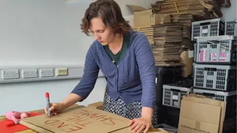 IRise International Emily Wilson, CEO of IRise International is making a protest sign which reads 'end the shame'