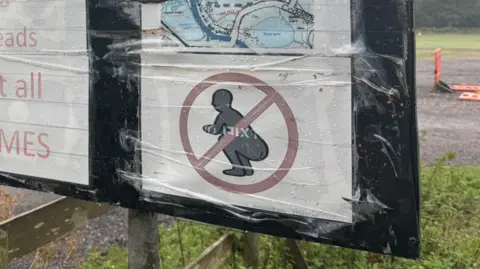 George King/BBC A close-up of a sign showing a figure squatting with a red circle around it.