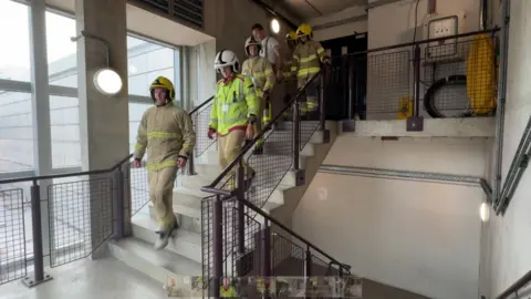 BBC Firefighters in full uniform walk up and down stairs as they train for the event