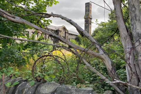 A shot of the back of Dalton Mills with barbed wire in the foreground