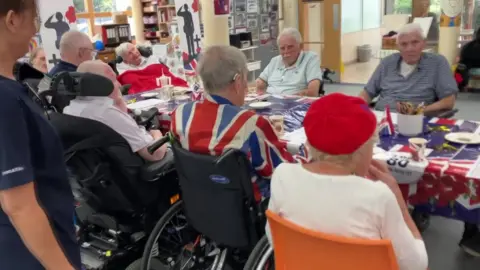 Royal Star & Garter care home for veterans in Worthing also held a special service for VJ Day. Veterans sitting around a table, decorated with Union Jack themed items.