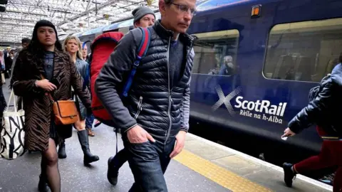 Commuters walking along a train platform next to a blue train with the ScotRail logo on it