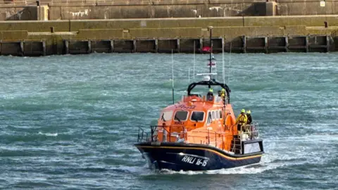 An orange lifeboat at sea with the Brighton Marina wall in the background