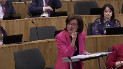 Senedd Cymru Eluned Morgan on her feet in the Senedd chamber gesticulating with her finger.
