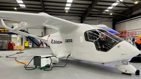White electric plane in a hangar. It has a large window at the front. On the side there are logos for "BETA Technologies" and eBristow.