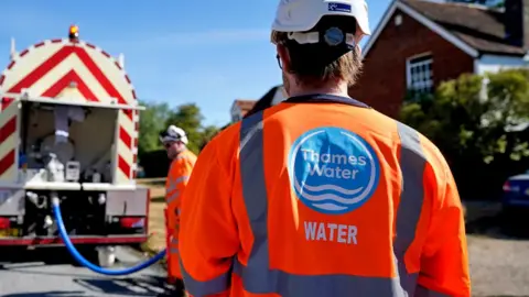 PA Media A worker from Thames Water delivering a temporary water supply from a tanker