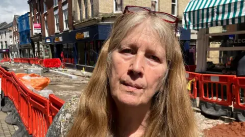 Alison Taylor standing near roadworks, with barriers on both sides of the road 