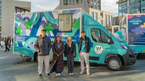 Four students stand in front of the bus decorated with the image they designed