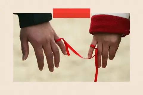 Getty Images Two people tie a red ribbon to their little fingers