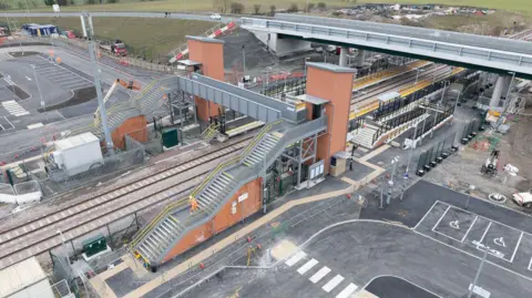 Northumberland County Council An aerial view of the new Newsham station which includes a road bridge, a large car park and a pedestrian bridge over the line.