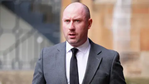 PA Media Neil Gray wearing a white shirt with a black tie under a grey suit.