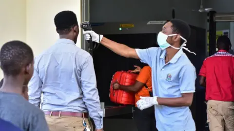 Getty Images A worker checks the temperature of travellers at the border post with Kenya in Namanga, northern Tanzania, on March 16, 2020, on the day Tanzania confirmed its first case of Covid-19.