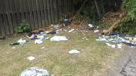 City of Wolverhampton Council A small piece of grass with a fence in the background. On the grass are items like packaging and plastic bottles.