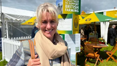 Minette Batters at an agricultural show. She is wearing a grey checked jacket and beige scarf.