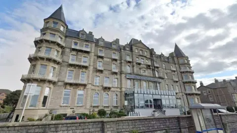 A Google Maps screengrab of the Grand Atlantic Hotel, a grey, five-storey Victorian building with pointy turrets and a glass entrance hall. 
