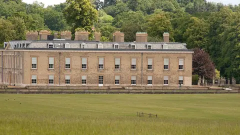 Getty Images A large stately home with a field in front of it and trees behind it.
