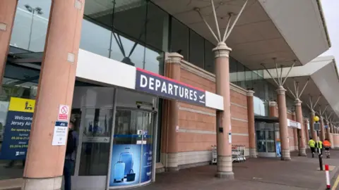 The exterior of part of Jersey Airport. In the foreground is a large revolving door with a sign saying "Departures".