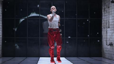 Olly Alexander performing on stage in red trousers and a white top