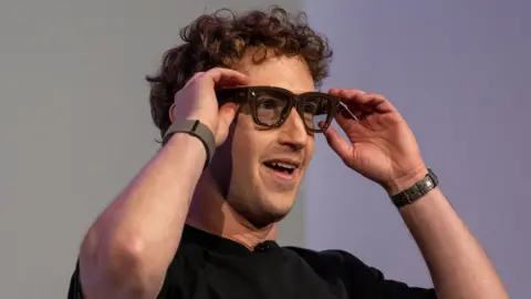 Getty Images A curly haired man in a dark shirt models a pair of heavy framed glasses