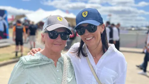 Kris Holland/BBC Two women in Ferrari baseball caps stand side-by-side on a bright and sunny day.