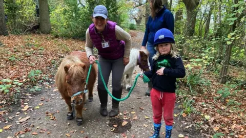 Emma leads a pony on a rein with a child to her left who is walking