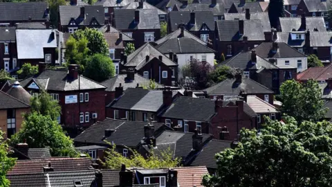Getty Images General view of Rotherham. A densely packed residential neighbourhood with rows of traditional brick houses. Most of the houses have dark, pitched roofs made of slate or tiles, and many feature chimneys.
Several houses have white-framed windows, and some display extensions or variations in roof shapes. The area is interspersed with greenery, visible between the houses and along the edges. In the background, more houses stretch into the distance.