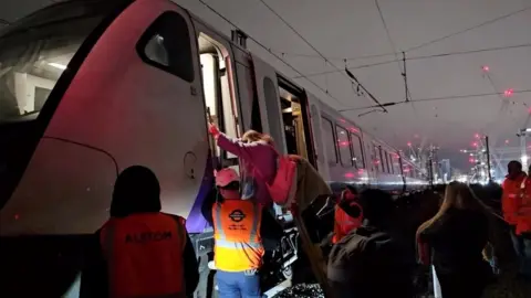 Reuters Officials assist passengers to get down from a train stuck on the Elizabeth line after damaged overhead cables blocked railway lines