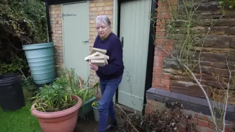 Juliet Jeater carries and armful blocks of wood she uses to heat her home from her shed.