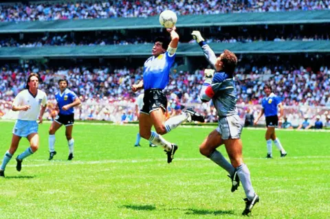 Bevilacqua Giuliano/ABACA/Shutterstock Diego Maradona handling the ball ahead of an approaching Peter Shilton