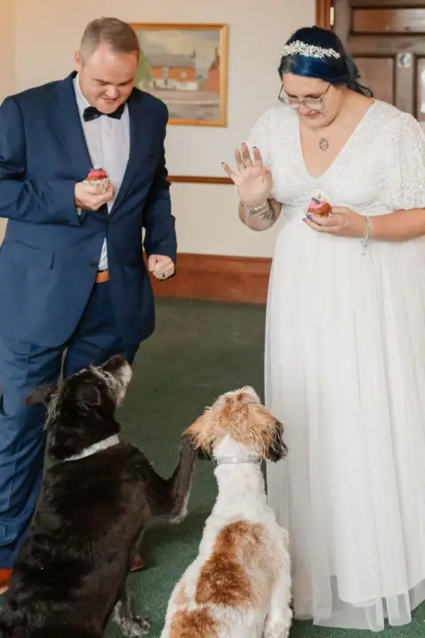 Victoria Jones Victoria Jones, in a white wedding dress, stands next to her husband Colin, in a suit, while their rescue dogs Biscuit and Scampi sit at their feet