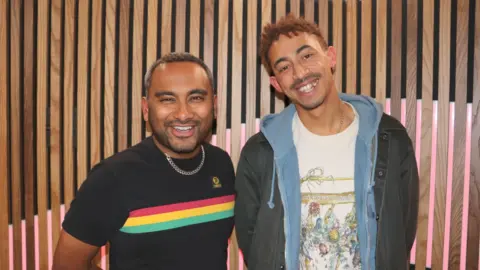 Two men, Amol Rajan and Jordan Stephens, stand side by side smiling. 