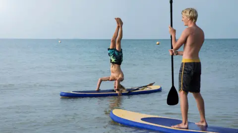 Getty Images Two men on paddle boards. One of them is doing a handstand.