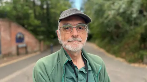 Claire Starr / BBC A man, Peter Burgess, stood wearing a green top, green shirt and a brown baseball cap.