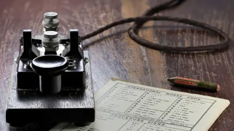 Getty Images Close up of Morse key, with Morse code chart on wooden desk.