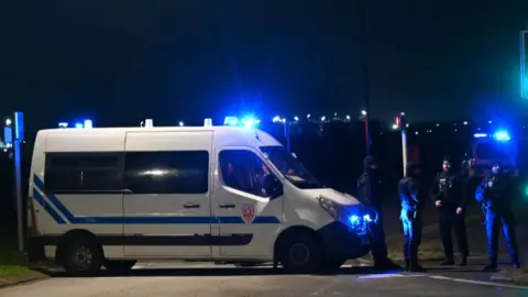 Getty French CRS Police (Republican Security Companies) block off a road near a migrant camp where two security guards and two migrants were shot dead, near Dunkirk, northern France, on December 14, 2024. Image shows a police van with blue flashing lights 