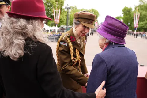 Getty Images Princess Anne smiles as she greets veterans while wearing brown military uniform and a hat, as the crowds gather around the Mall.