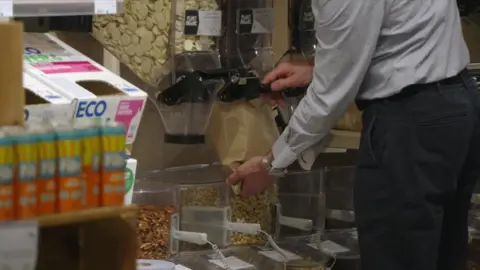 A person fills a brown paper bag with dried good at Planet Organic