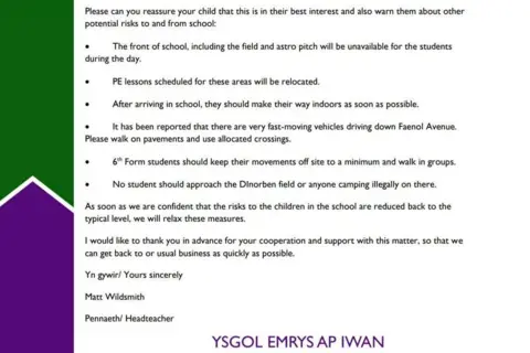 Ysgol Emrys Ap Iwan The letter from the head teacher to parents. There is a green and purple indent on the left, with the text formatted on the right.
The letter continues:
Please can you reassure your child that this is in their best interest and also warn them about other potential risks to and from school:
The front of school, including the field and astro pitch will be unavailable for the students during the day.
PE lessons scheduled for these areas will be relocated.
After arriving in school, they should make their way indoors as soon as possible.
It has been reported that there are very fast-moving vehicles driving down Faenol Avenue. Please walk on pavements and use allocated crossings.
6th Form students should keep their movements off site to a minimum and walk in groups.
No student should approach the Dinorben field or anyone camping illegally on there.
As soon as we are confident that the risks to the children in the school are reduced back to the typical level, we will relax these measures. I would like to thank you in advance for your cooperation and support with this matter, to that we can get back to or usual business as quickly as possible.
Yn gywir/ Yours sincerely
Matt Wildsmith
Pennaeth/ Headteacher