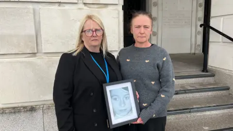 Lisa Morris, left, and Roisin Morris, right, pictured outside Parliament Buildings, Stormont, holding a photograph of their mother Madeline