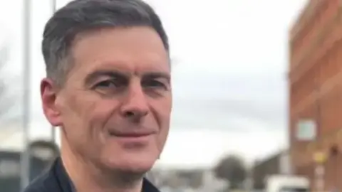 Shows a man in a black t-shirt and black jacket