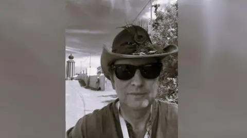 Stuart Saunders A black and white photograph of a man wearing sunglasses and a cowboy hat