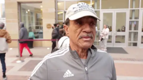 Kevin Williams wears a baseball cap and tracksuit top as he speaks outside an evacuation centre