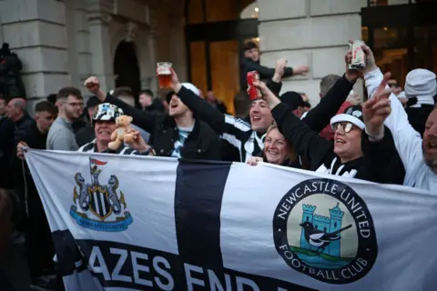 HENRY NICHOLLS/Getty Images A group of fans with a Newcastle United flag in Covent Garden looking happy and excited.