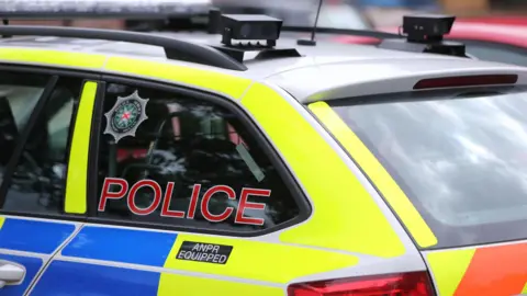 Blue, yellow and red vehicle with red police label on the window and PSNI crest.