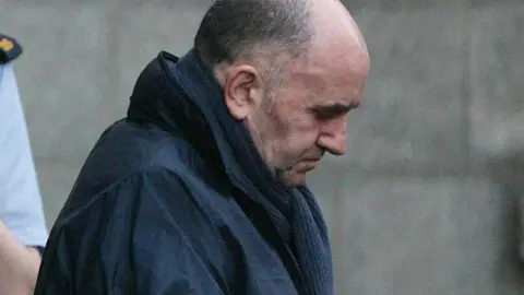 PA/Niall Carson Michael McKevitt leaving Dublin"s Supreme Court after he began an appeal against his conviction for directing terrorism in 2008.  He is balding with dark, greying hair and is wearing a navy coat and scarf. 