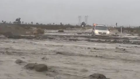 Muddy water is streaming down in California with a car seen.