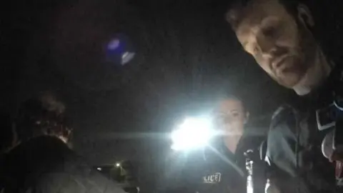 Picture of two police officers, on of which is holding a torch. You can also see the back of a mans head. 