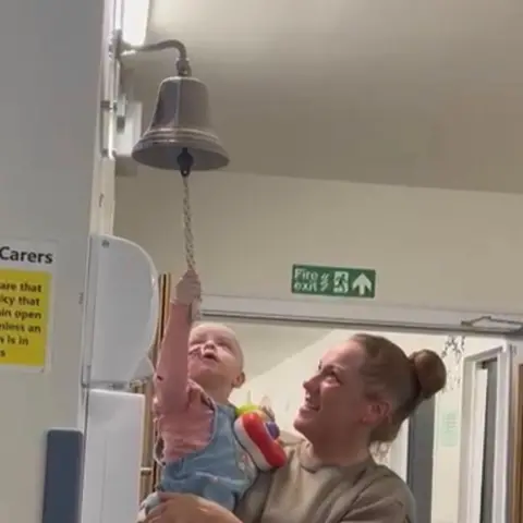 Supplied A young girl reaching up to ring a bell on the wall of a hospital ward