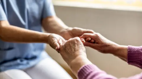 Stock close-up image of a nurse holding an elderly person's hands.