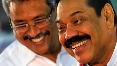 AFP Sri Lankan President Mahinda Rajapakse (R) and Sri Lankan Defence Ministry Secretary Gotabaya Rajapaksa (L) walk past Buddhist monks during the War Heroes religion ceremony in Colombo on May 9, 2013.